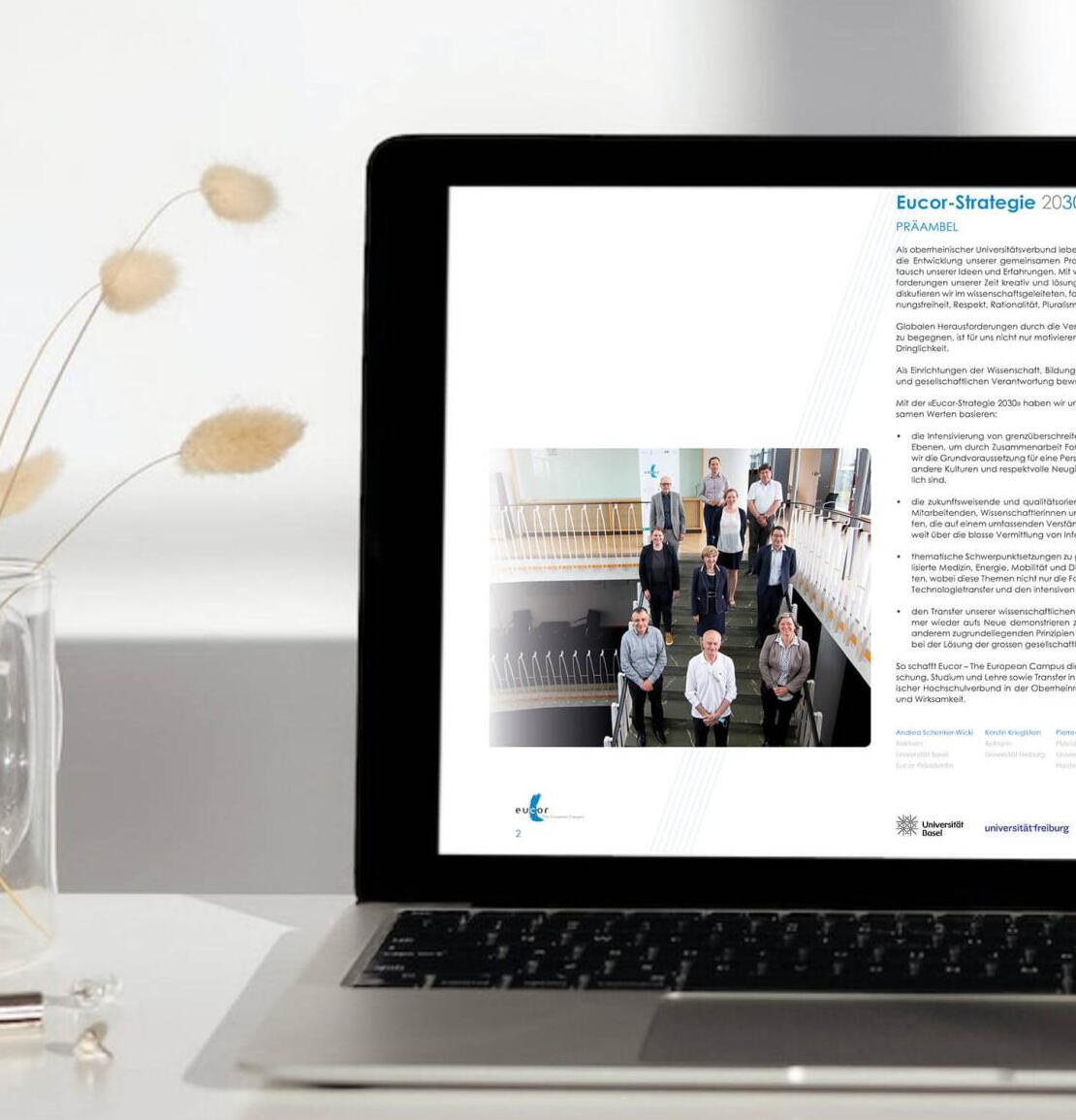 Stratégie d'Eucor 2030 Un ordinateur portable est posé sur un bureau avec un vase et un verre d'eau.